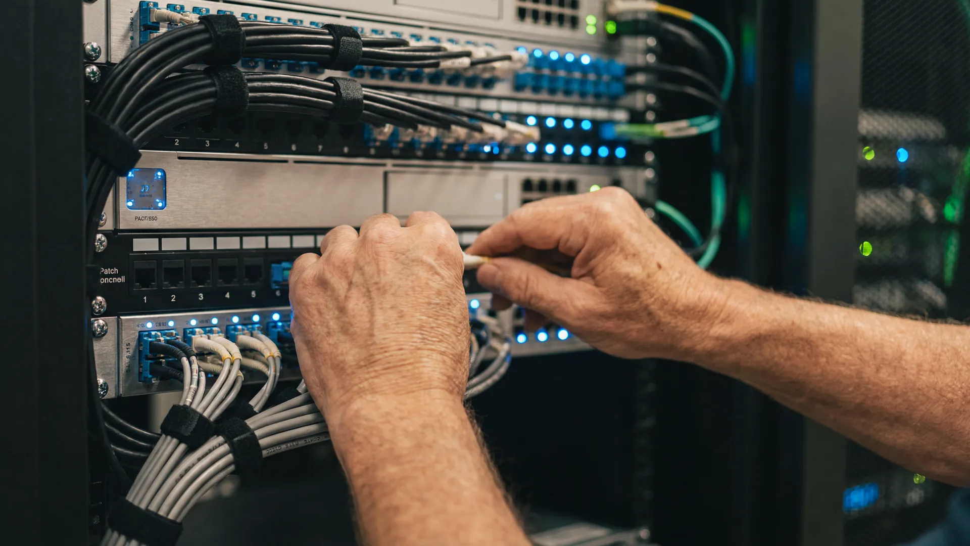 M&atilde;os experientes de um engenheiro conectando fibra &oacute;ptica em um painel de telecomunica&ccedil;&otilde;es